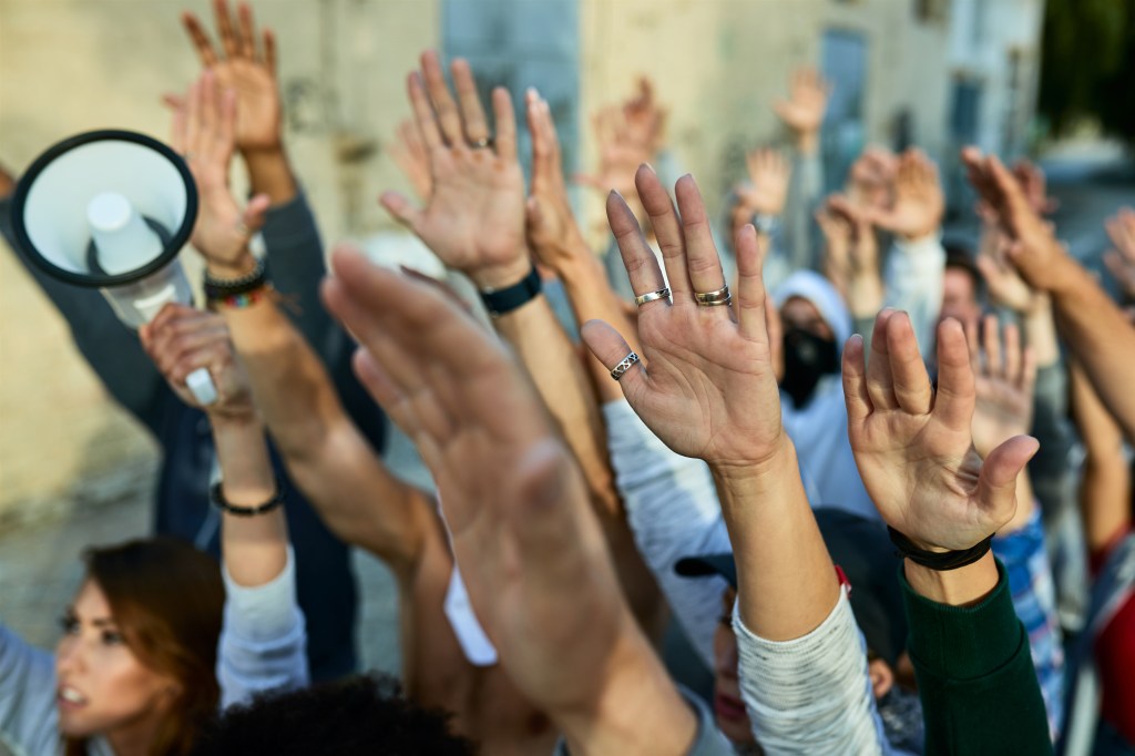 Des mains levées en signe de solidarité lors d'une manifestation, avec un mégaphone visible en arrière-plan.